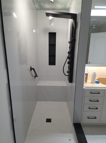 Bathroom renovation in Toronto featuring a modern walk-in shower with custom tile, built-in shelf, black fixtures, and safety grab bar by a professional contractor.